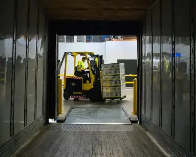 A man driving a forklift and using it to carry boxes